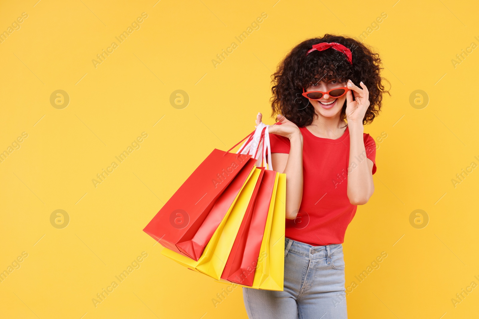 Photo of Happy young woman with shopping bags and stylish sunglasses on yellow background. Space for text