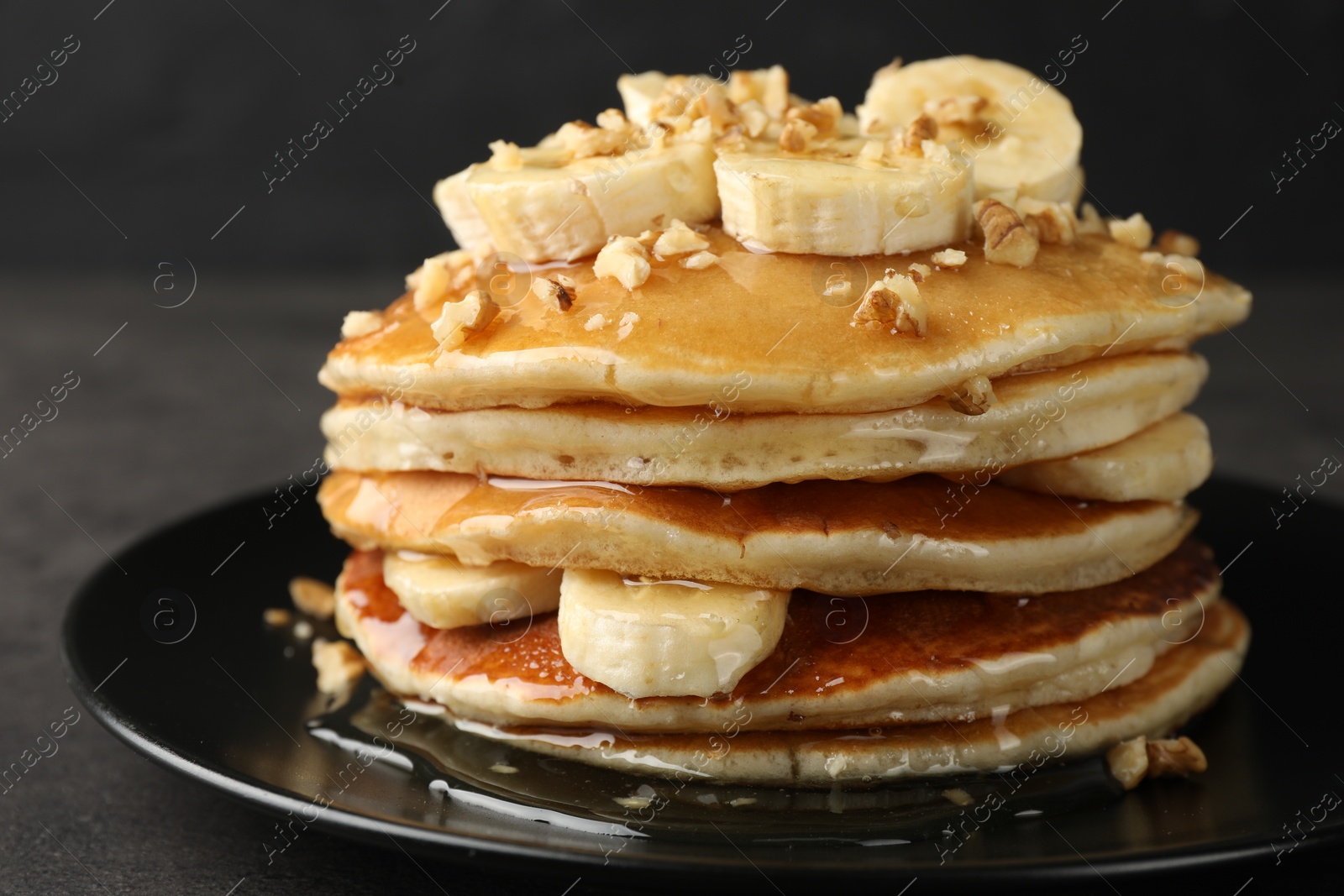 Photo of Delicious pancakes with bananas, walnuts and honey on dark table, closeup