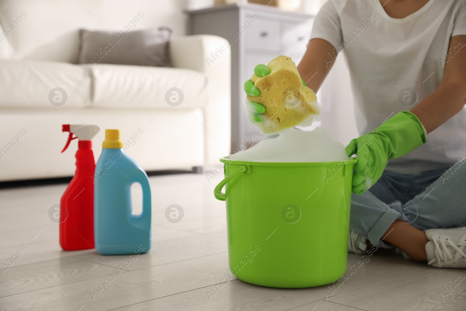 Photo of Woman holding sponge with foam over bucket indoors, closeup. Cleaning supplies