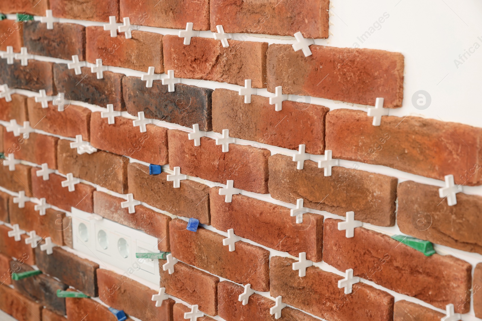 Photo of Decorative bricks with tile leveling system on white wall in room