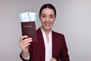 Smiling businesswoman showing passport and tickets on grey background, selective focus