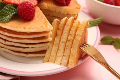 Photo of Eating delicious pancakes with raspberry, honey and fork at pink table, closeup