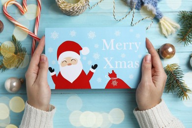 Photo of Woman holding Christmas card at light blue wooden table, top view