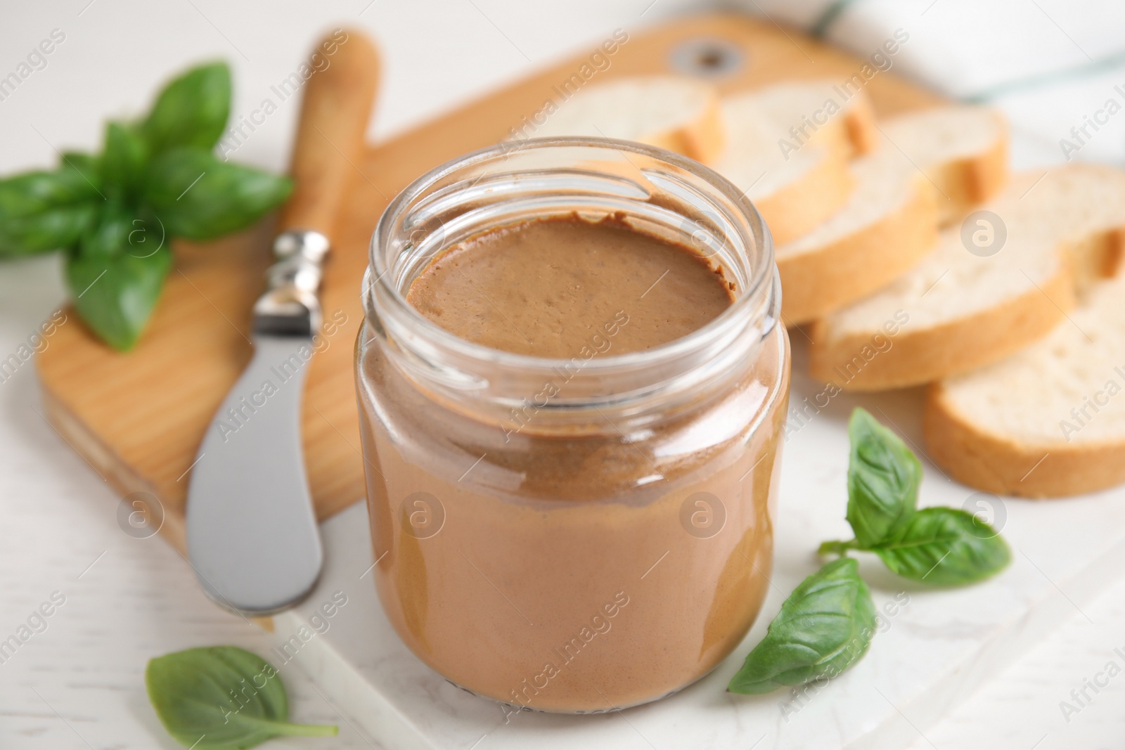 Photo of Delicious meat pate, fresh bread, knife and basil on white wooden table, closeup