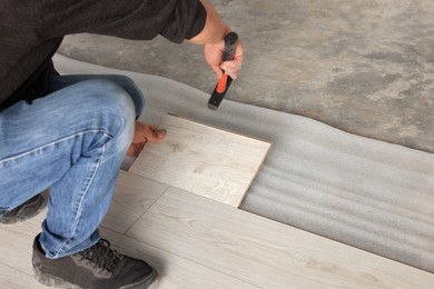 Photo of Professional worker using hammer during installation of new laminate flooring, closeup. Space for text
