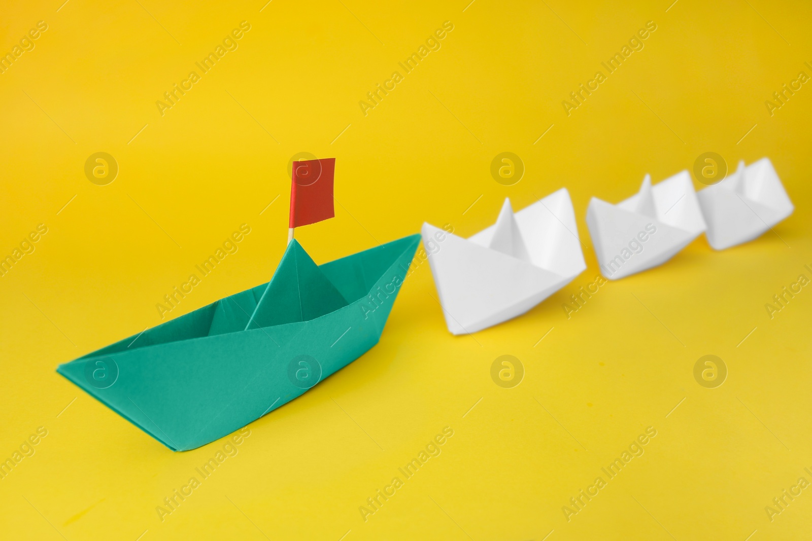 Photo of Group of paper boats following green one on yellow background. Leadership concept