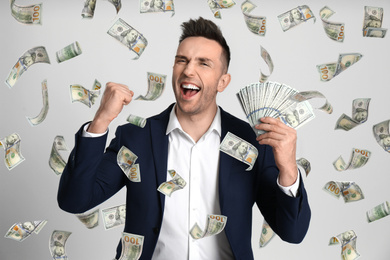 Image of Happy young man with dollars under money rain on light background