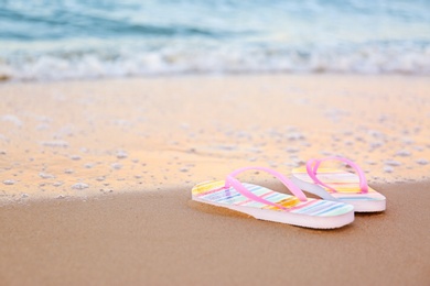 Photo of Stylish flip flops on sand near sea, space for text. Beach accessories