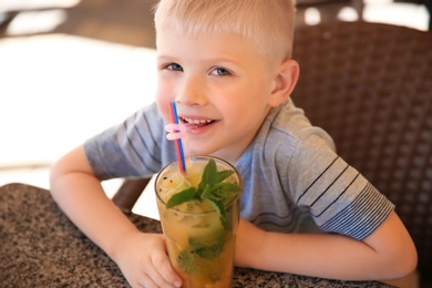 Photo of Cute boy with glass of natural lemonade at table in cafe