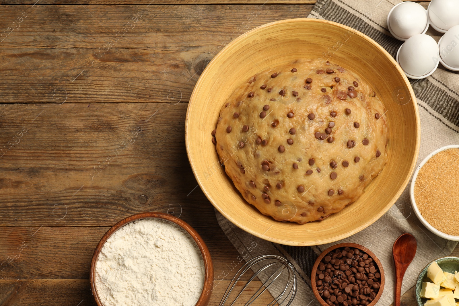 Photo of Bowl with dough and ingredients for cooking chocolate chip cookies on wooden table, flat lay. Space for text