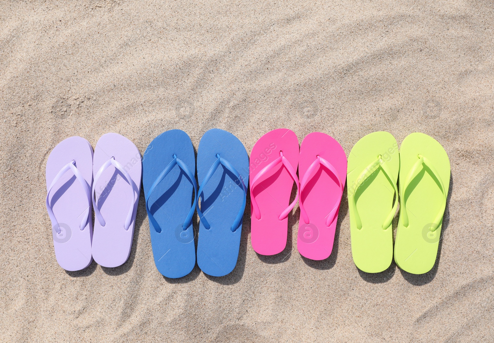 Photo of Many stylish colorful flip flops on sand outdoors, flat lay