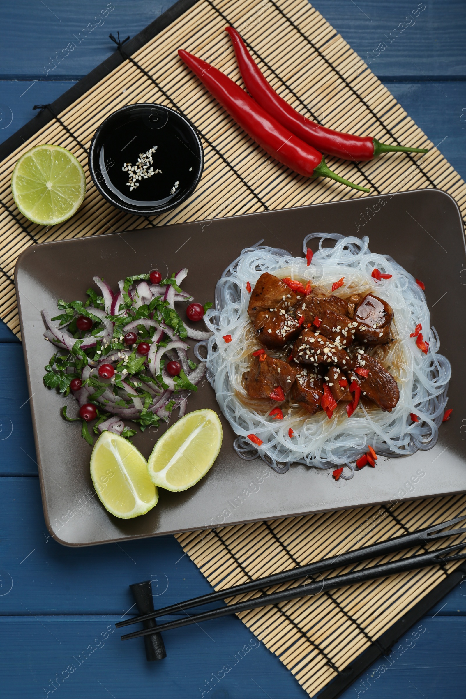 Photo of Pieces of soy sauce chicken with noodle, salad and lime served on blue wooden table, flat lay