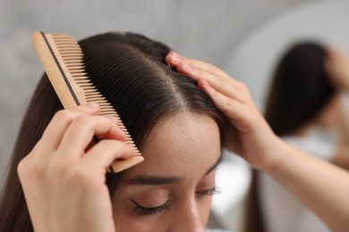 Photo of Woman with comb examining her hair and scalp on blurred background, closeup