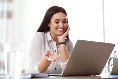 Photo of Young woman using video chat on laptop in home office