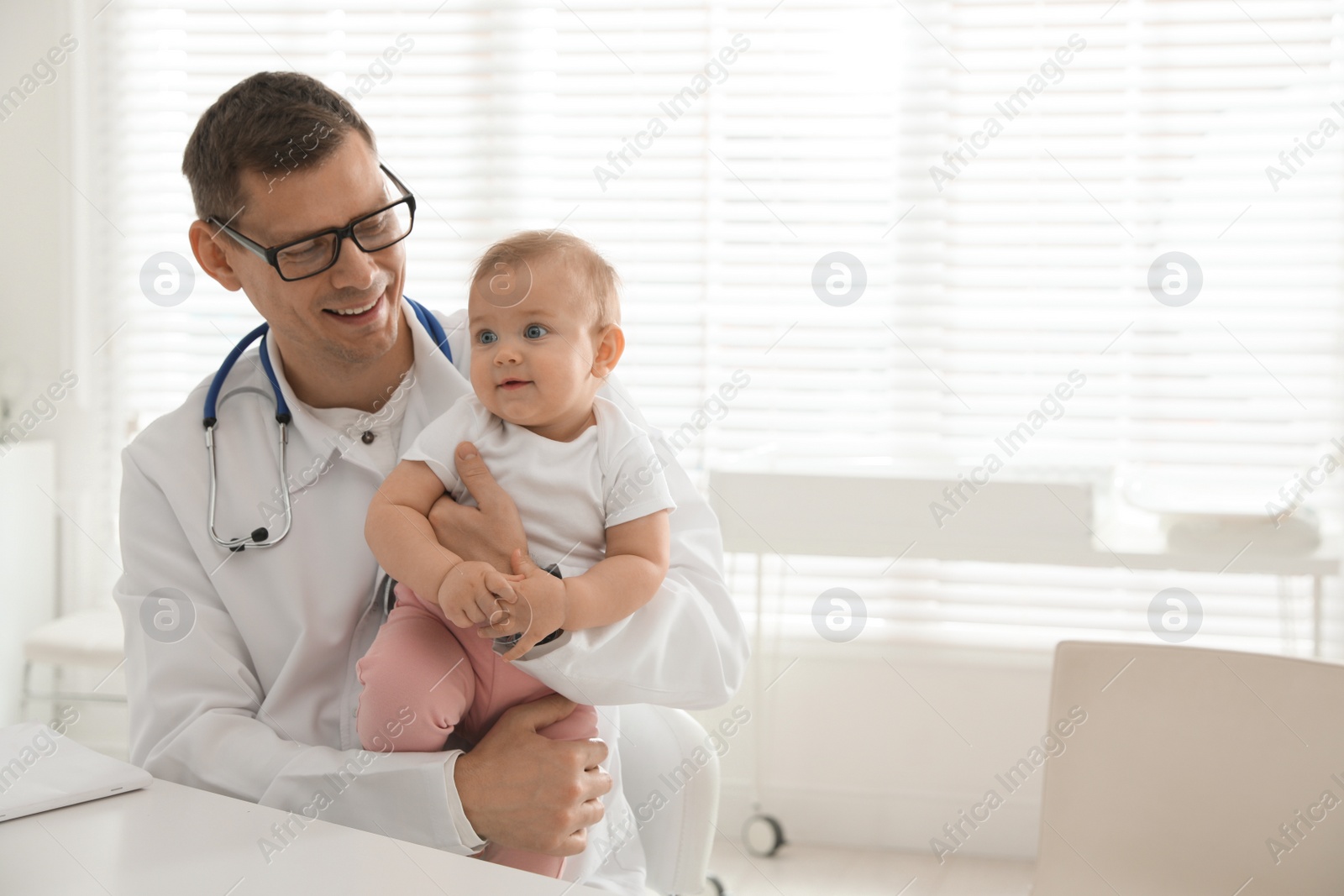 Photo of Pediatrician with cute little baby in clinic. Space for text
