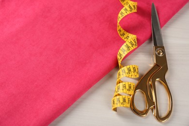 Photo of Scissors, tape measure and pink fabric on light beige wooden table. Space for text