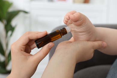 Photo of Mother applying essential oil from roller bottle onto her baby`s heel indoors, closeup