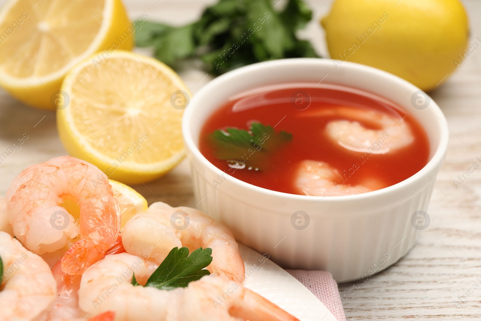 Photo of Tasty boiled shrimps with cocktail sauce, chili and parsley on light wooden table, closeup