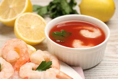 Photo of Tasty boiled shrimps with cocktail sauce, chili and parsley on light wooden table, closeup