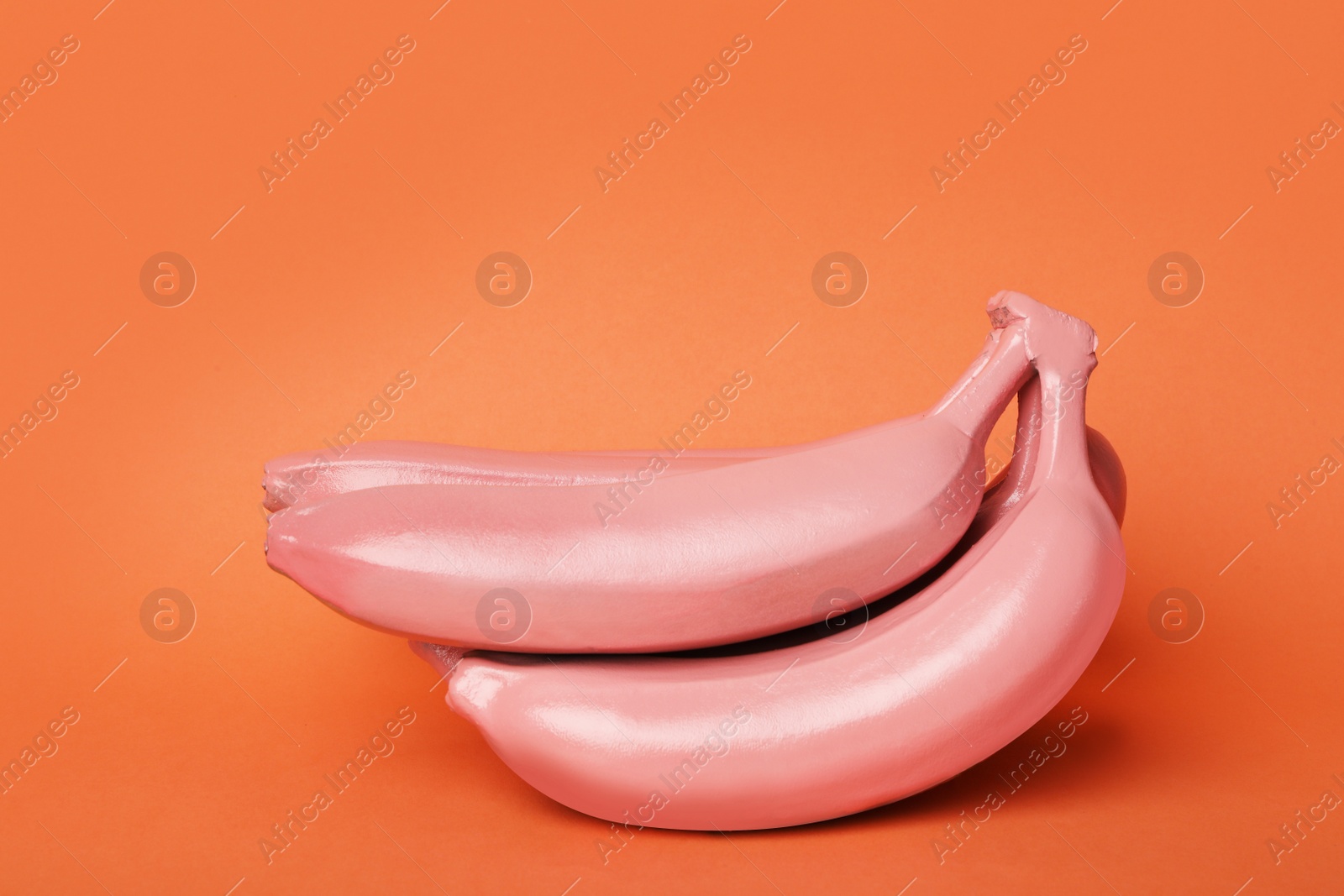 Photo of Coral painted raw bananas on orange background