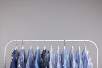 Photo of Dry-cleaning service. Many different clothes in plastic bags hanging on rack against grey background, space for text