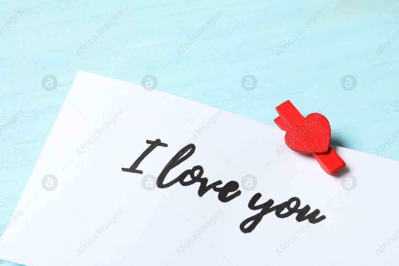 Photo of Card with text I Love You and red clothespin on light blue wooden background, closeup