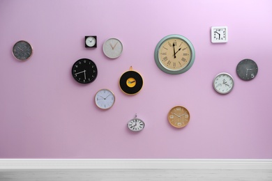 Photo of Many different clocks hanging on color wall. Time of day
