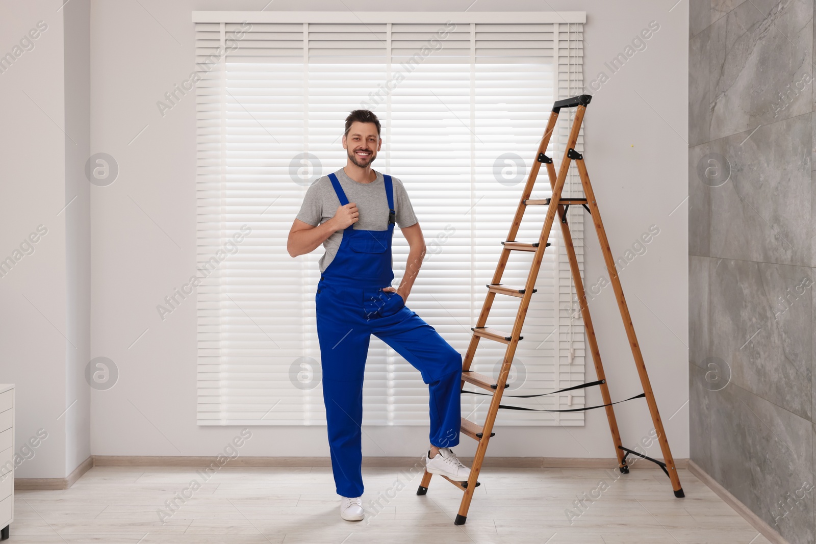 Photo of Worker in uniform and stepladder near horizontal window blinds indoors