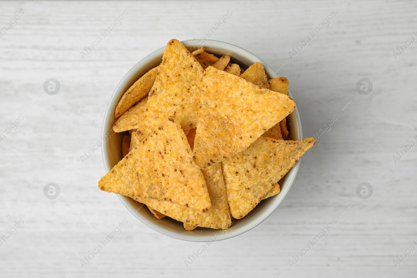 Photo of Bowl with tasty Mexican nachos chips on white wooden table, top view