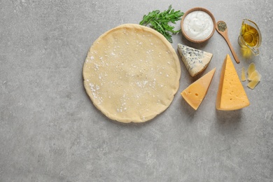 Flat lay composition with pizza crust and fresh ingredients on grey table. Space for text