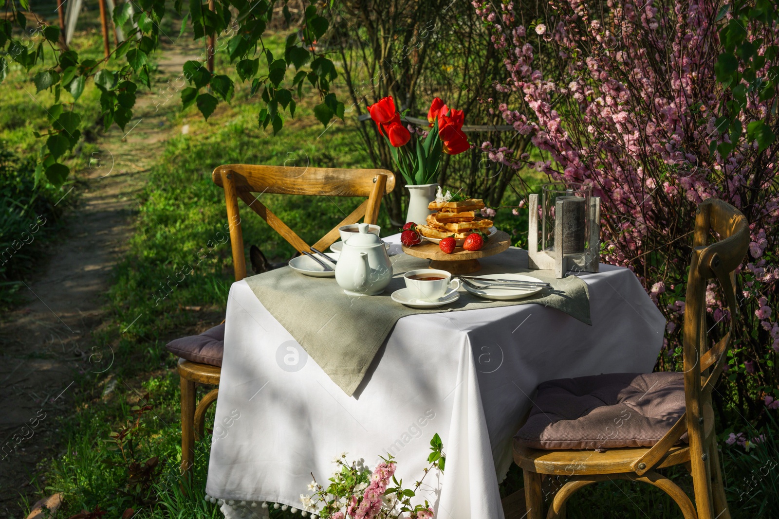 Photo of Beautiful bouquet of tulips and freshly baked waffles on table served for tea drinking in garden