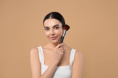 Photo of Portrait of beautiful woman with makeup brush on light brown background