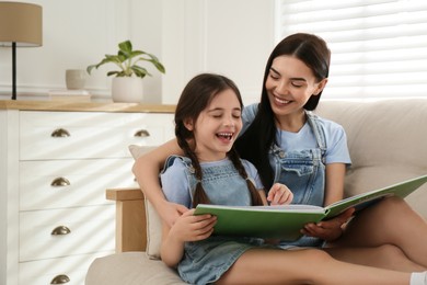 Photo of Young mother and her daughter reading book on sofa at home, space for text