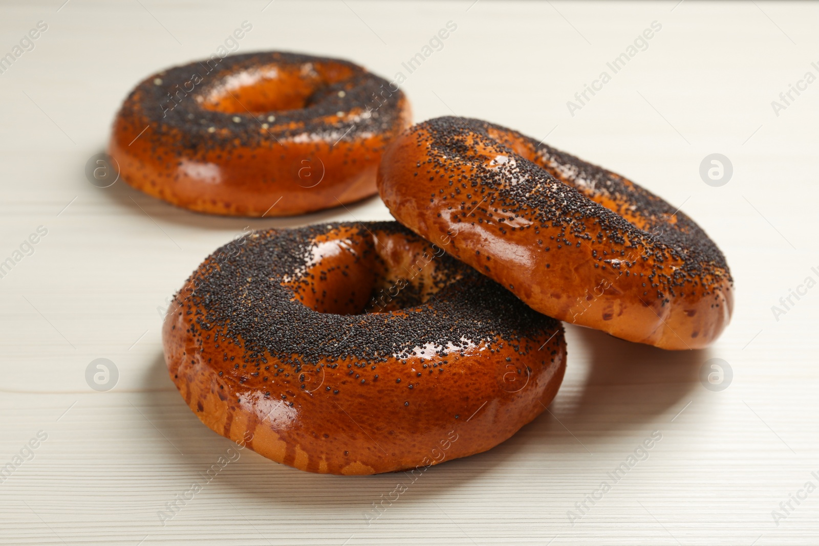 Photo of Delicious fresh bagels with poppy seeds on white wooden table