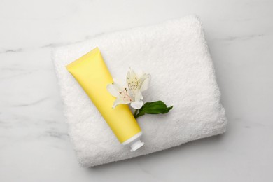 Cosmetic product, flower and fresh towel on white marble table, top view. Spa composition