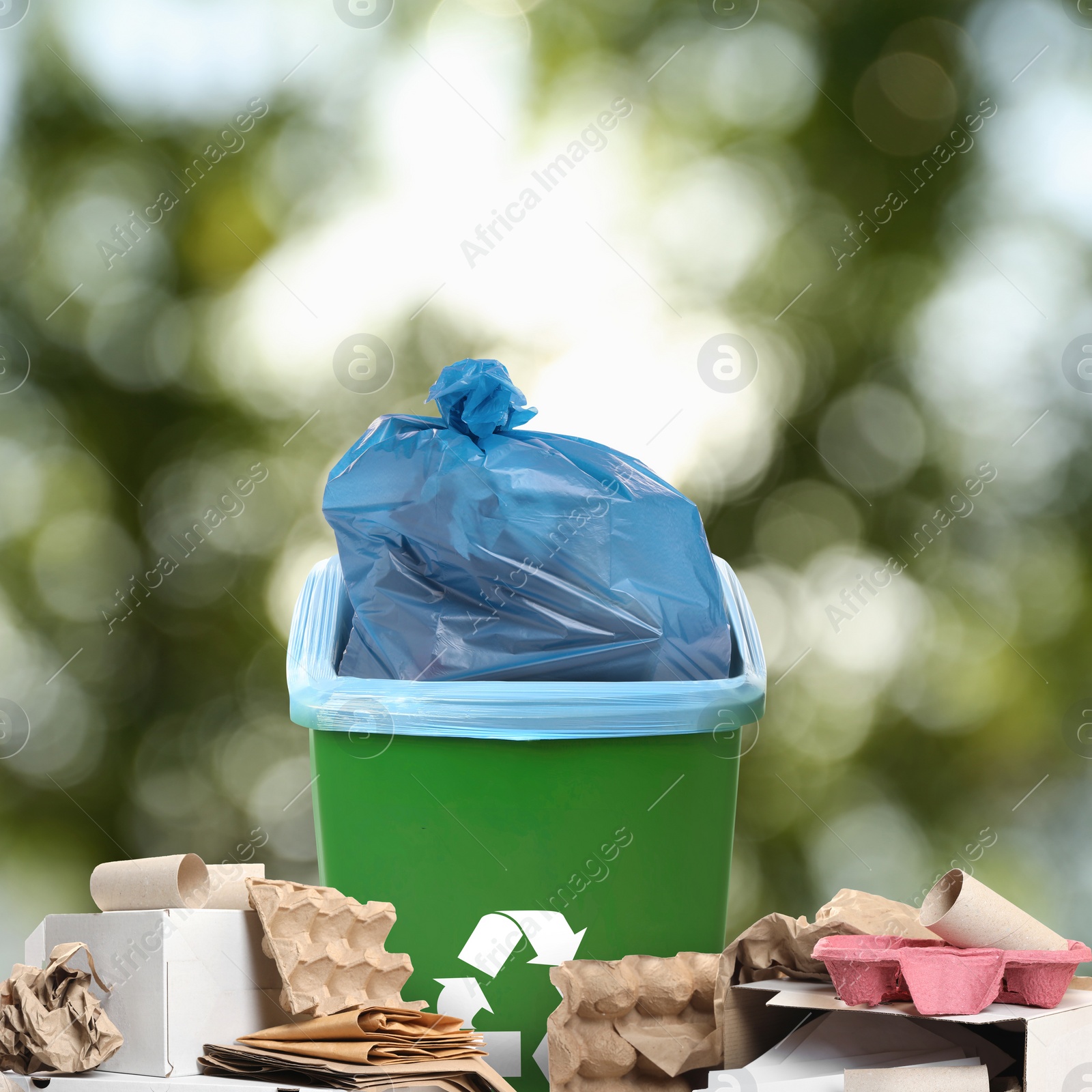 Image of Waste bin with plastic bag full of trash surrounded by garbage on blurred background