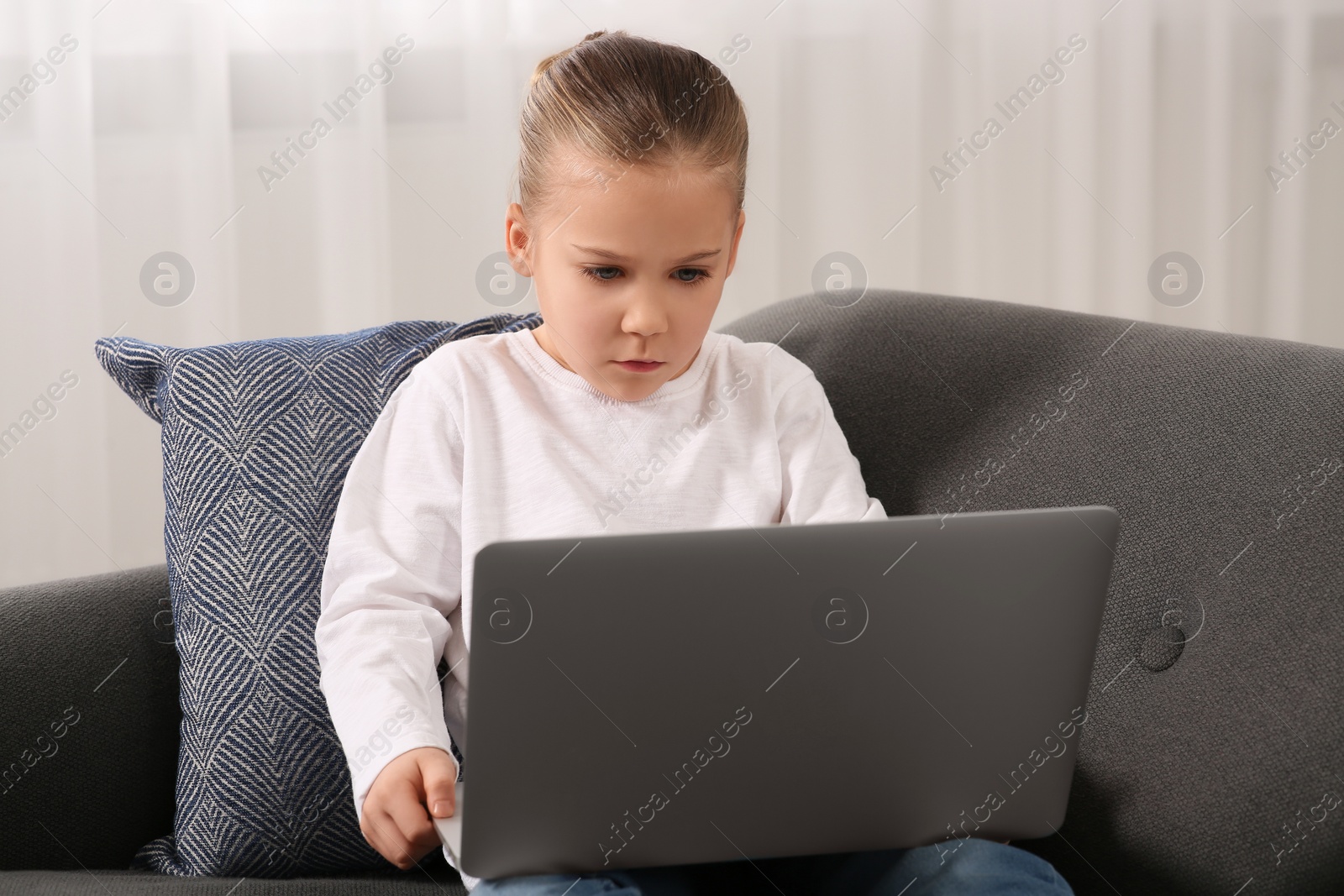 Photo of Little girl using laptop on sofa at home. Internet addiction