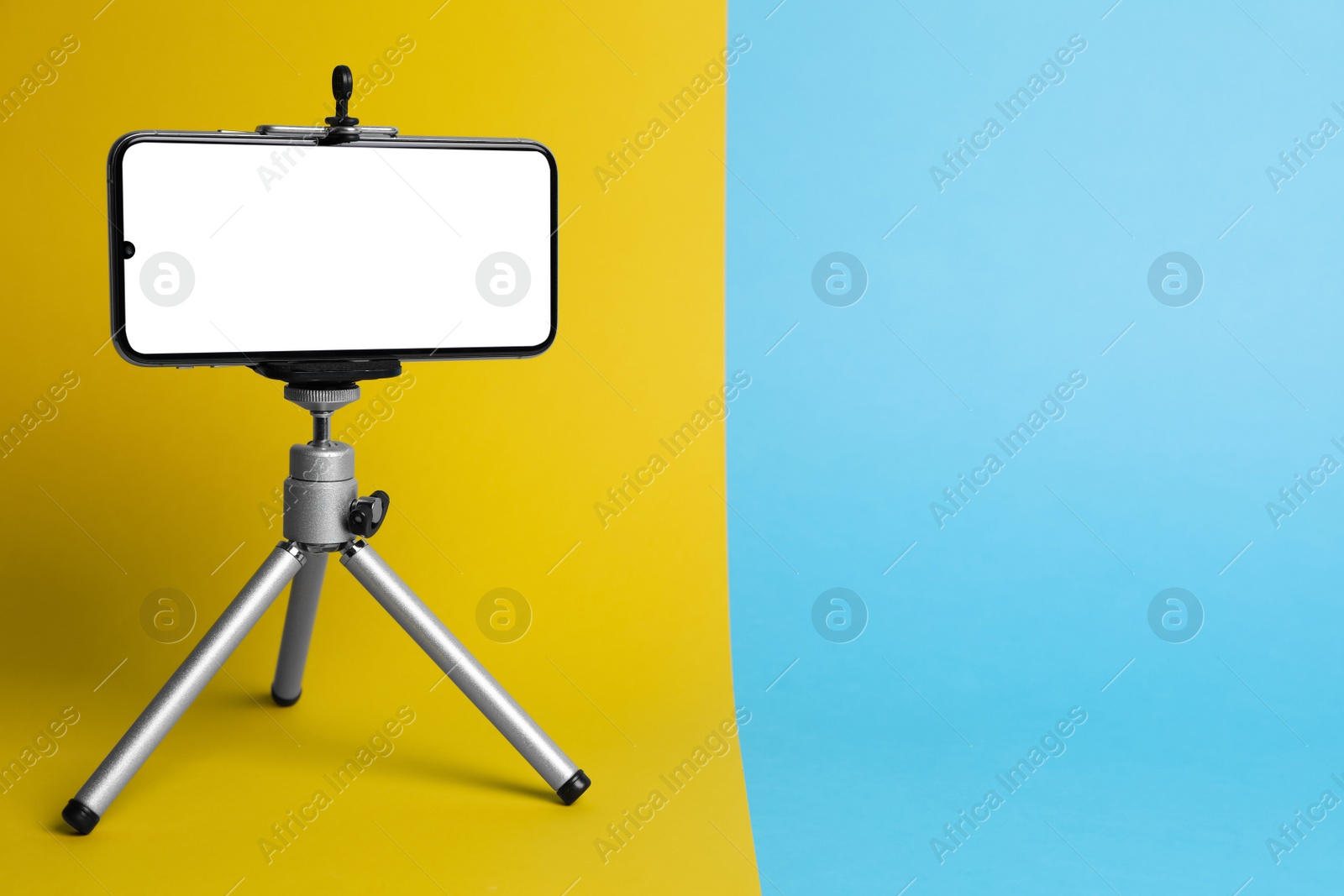 Photo of Modern tripod with smartphone on color background. Space for text