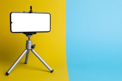 Photo of Modern tripod with smartphone on color background. Space for text