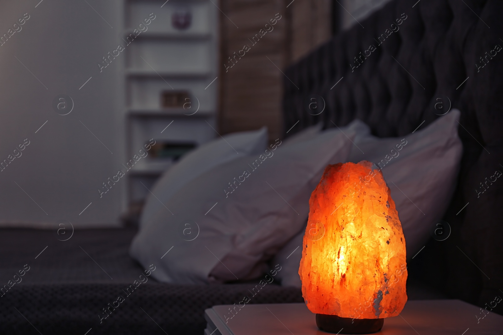 Photo of Himalayan salt lamp on bedside table against blurred background with space for text