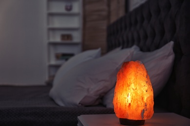 Photo of Himalayan salt lamp on bedside table against blurred background with space for text