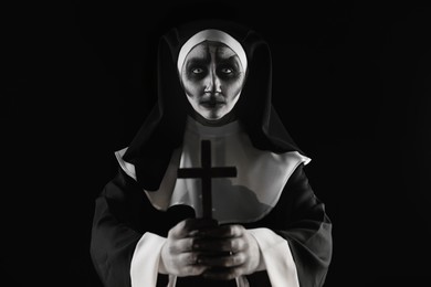 Photo of Scary devilish nun with cross on black background. Halloween party look