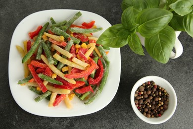 Mix of different frozen vegetables, basil and spices on gray table, flat lay