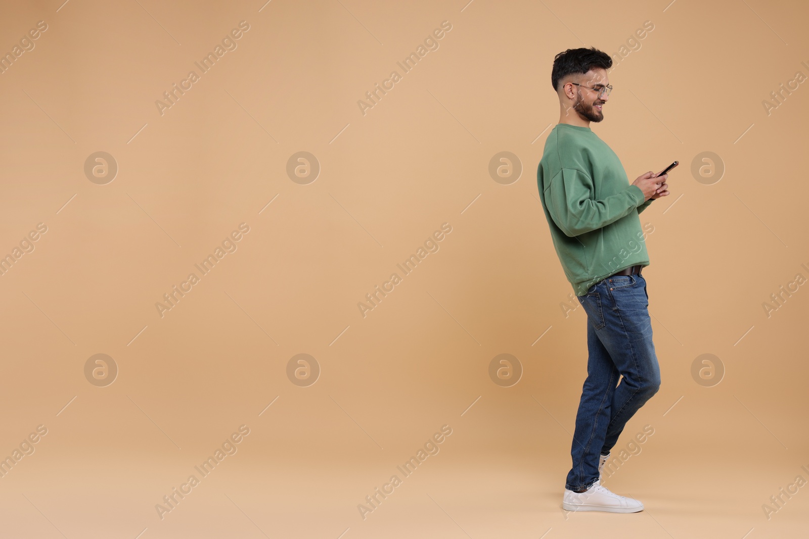 Photo of Handsome young man using smartphone on beige background, space for text