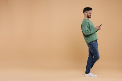 Handsome young man using smartphone on beige background, space for text