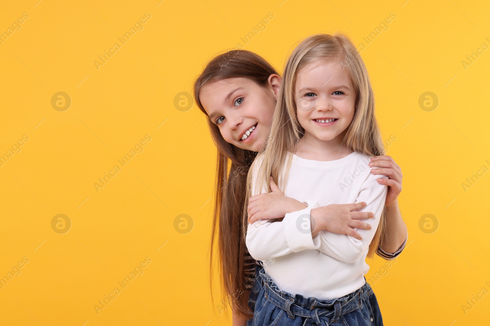 Photo of Portrait of cute little sisters on orange background, space for text