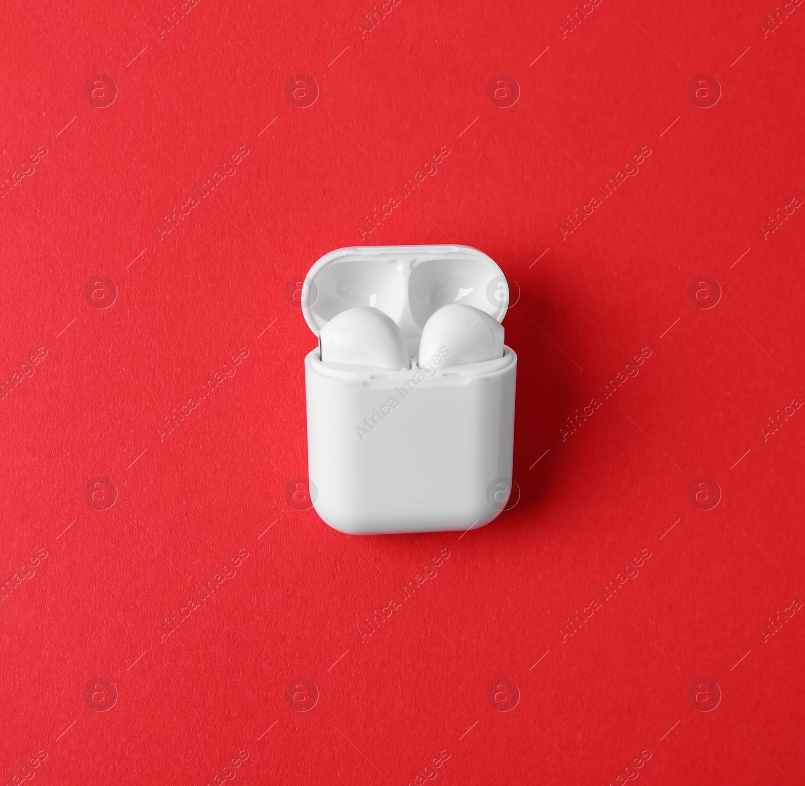 Photo of Modern wireless earphones in charging case on red background, top view