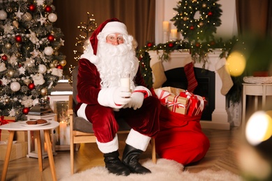 Santa Claus with glass of milk in room decorated for Christmas
