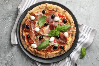 Photo of Tasty pizza with cured ham, olives, mozzarella cheese, sun-dried tomato and basil on gray textured table, top view