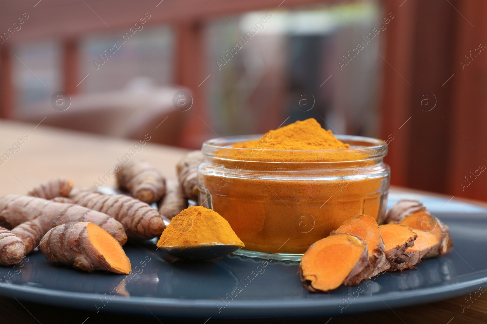 Photo of Plate with glass jar of turmeric powder and fresh roots on table